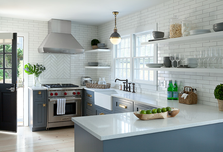 Inspiration for a mid-sized beach style u-shaped eat-in kitchen in New York with a farmhouse sink, shaker cabinets, grey cabinets, quartz benchtops, white splashback, subway tile splashback, stainless steel appliances, light hardwood floors and no island.