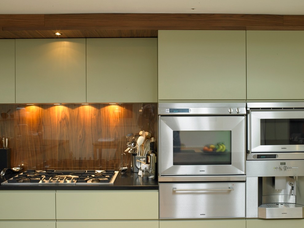 Mid-sized contemporary open plan kitchen in London with an integrated sink, flat-panel cabinets, green cabinets, granite benchtops, glass sheet splashback, stainless steel appliances, porcelain floors and with island.