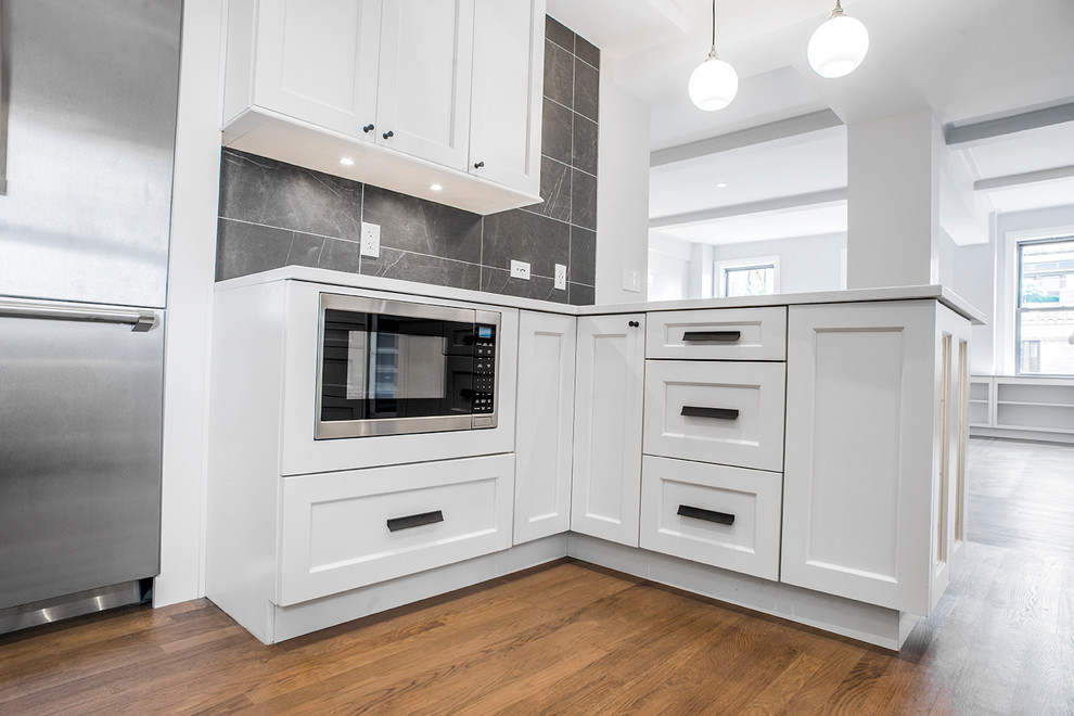 Inspiration for a large contemporary eat-in kitchen in New York with an undermount sink, shaker cabinets, white cabinets, quartz benchtops, black splashback, porcelain splashback, stainless steel appliances, medium hardwood floors and a peninsula.