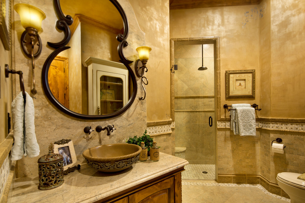 Design ideas for a mid-sized mediterranean 3/4 bathroom in Dallas with a vessel sink, medium wood cabinets, granite benchtops, an alcove shower, a one-piece toilet, mosaic tile, beige walls, ceramic floors, furniture-like cabinets, beige tile, beige floor, a hinged shower door and beige benchtops.