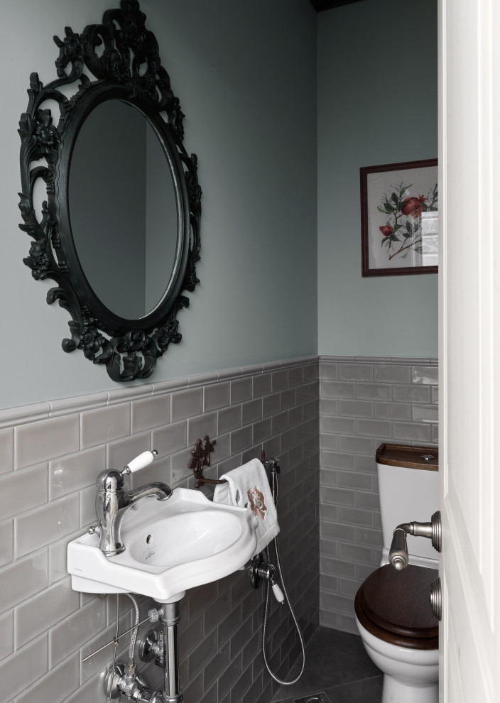 Bild på ett litet vintage vit vitt toalett, med en toalettstol med hel cisternkåpa, grå kakel, keramikplattor, grå väggar, klinkergolv i keramik, ett väggmonterat handfat, kaklad bänkskiva och grått golv