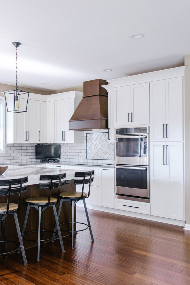 Example of a mid-sized transitional l-shaped medium tone wood floor and brown floor eat-in kitchen design in Omaha with a farmhouse sink, shaker cabinets, white cabinets, quartzite countertops, white backsplash, subway tile backsplash, stainless steel appliances, an island and white countertops