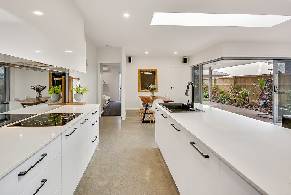 Large contemporary single-wall eat-in kitchen in Sunshine Coast with a drop-in sink, white cabinets, quartzite benchtops, black splashback, white appliances, concrete floors, with island and mirror splashback.