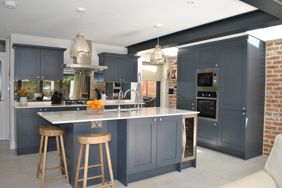 Mid-sized contemporary l-shaped kitchen in London with a double-bowl sink, recessed-panel cabinets, blue cabinets, quartzite benchtops, mirror splashback, stainless steel appliances, with island, grey floor and white benchtop.