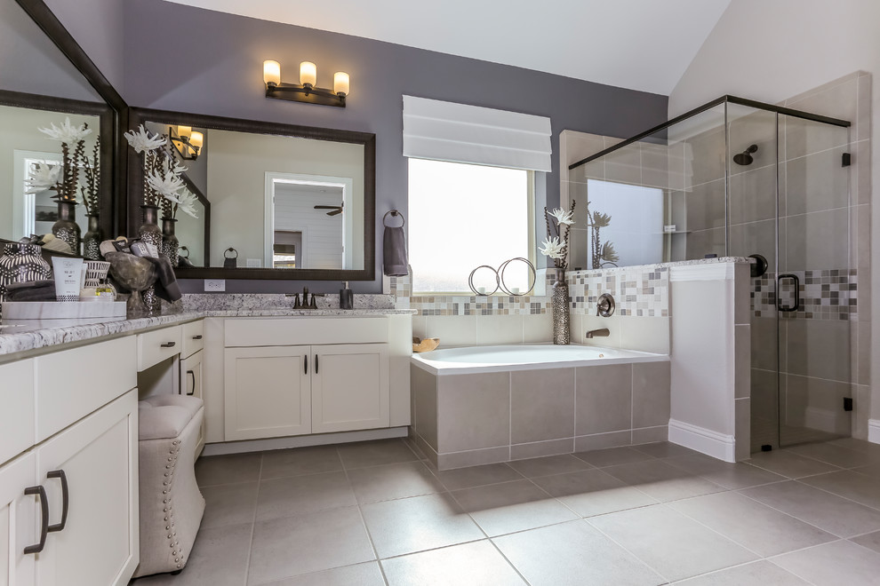 This is an example of a large country master bathroom in Houston with recessed-panel cabinets, white cabinets, a drop-in tub, a corner shower, beige tile, stone tile, grey walls, ceramic floors, an undermount sink, granite benchtops, beige floor and a hinged shower door.