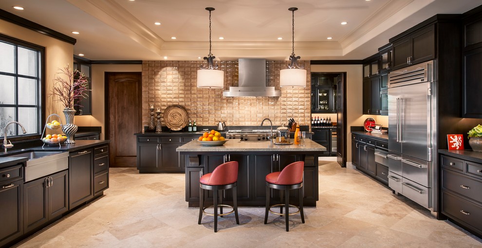 Photo of an expansive contemporary u-shaped kitchen in Phoenix with a farmhouse sink, recessed-panel cabinets, dark wood cabinets, beige splashback, stainless steel appliances, limestone floors, with island, granite benchtops, porcelain splashback and beige floor.