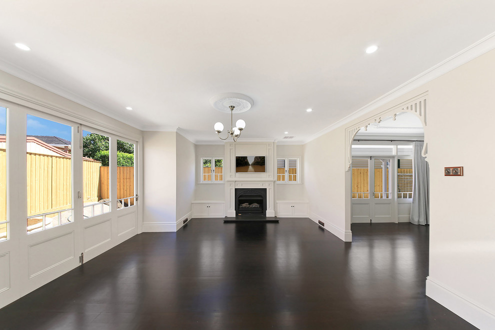 This is an example of a large transitional formal open concept living room in Sydney with dark hardwood floors, a standard fireplace, a wood fireplace surround, a wall-mounted tv, white walls and brown floor.