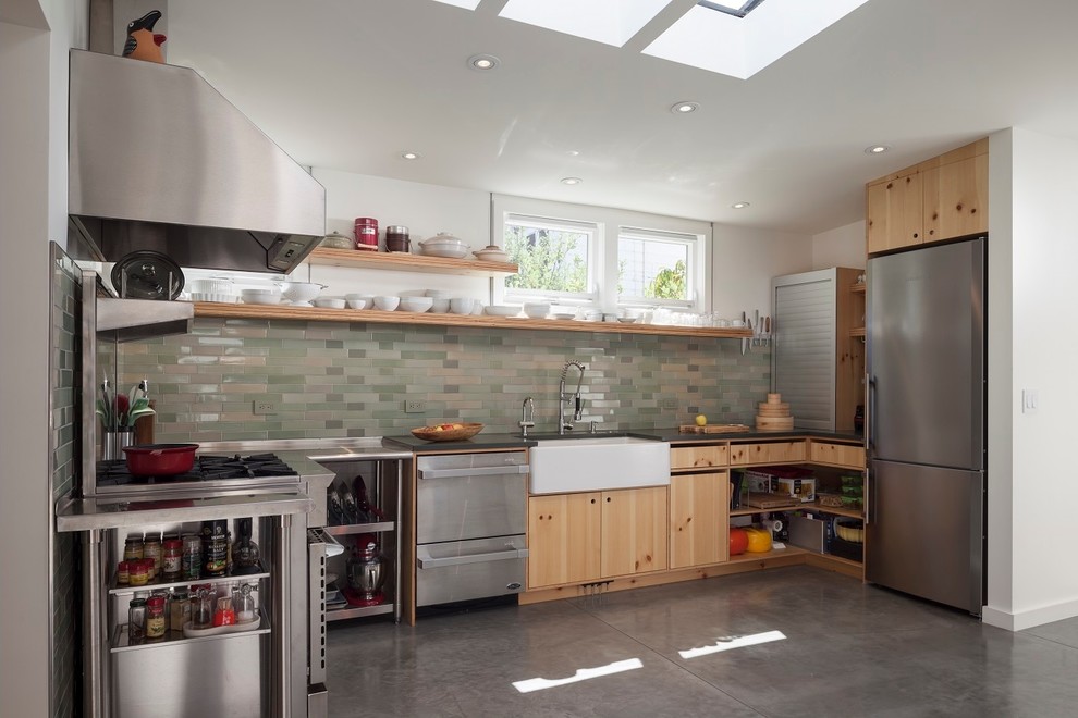 Inspiration for a mid-sized contemporary u-shaped concrete floor and gray floor kitchen remodel in San Francisco with a farmhouse sink, flat-panel cabinets, light wood cabinets, green backsplash, glass tile backsplash, stainless steel appliances, no island and black countertops