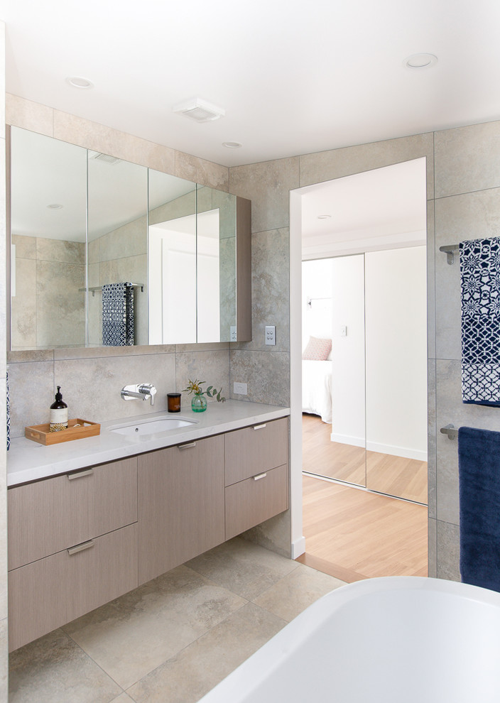 This is an example of a small contemporary master bathroom in Other with furniture-like cabinets, light wood cabinets, a freestanding tub, an open shower, a one-piece toilet, white tile, ceramic tile, beige walls, ceramic floors, an undermount sink and engineered quartz benchtops.