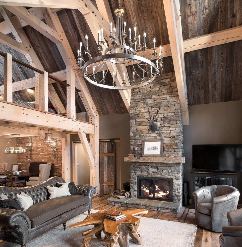 This is an example of a large country open concept living room in Atlanta with grey walls, medium hardwood floors, a standard fireplace, a stone fireplace surround and a freestanding tv.