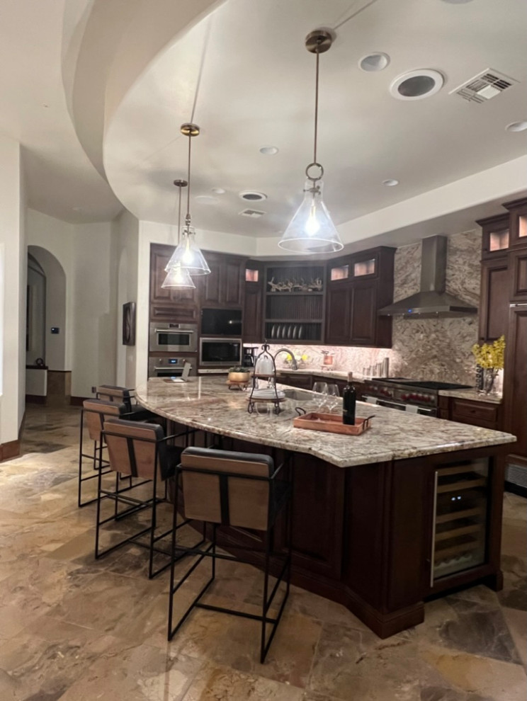 This is an example of an expansive kitchen in Phoenix with a double-bowl sink, glass-front cabinets, dark wood cabinets, granite benchtops, grey splashback, stone slab splashback, stainless steel appliances, travertine floors, with island, beige floor, grey benchtop and recessed.