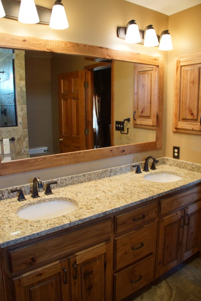 This is an example of a mid-sized country master bathroom in Other with raised-panel cabinets, medium wood cabinets, an alcove shower, a one-piece toilet, multi-coloured tile, stone tile, beige walls, travertine floors, an undermount sink and granite benchtops.