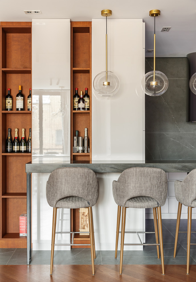 Inspiration for a contemporary home bar in Moscow with flat-panel cabinets, white cabinets, solid surface benchtops, grey benchtop and grey splashback.