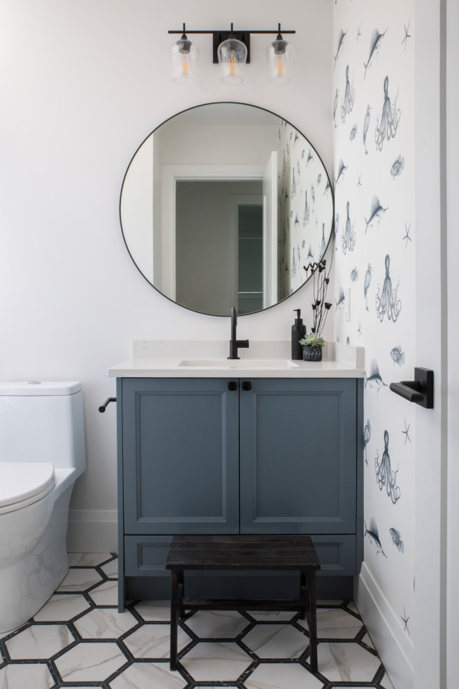 Inspiration for a transitional powder room in Vancouver with grey cabinets, a one-piece toilet, white walls, an undermount sink, multi-coloured floor, white benchtops, a built-in vanity, wallpaper, shaker cabinets, porcelain floors and engineered quartz benchtops.