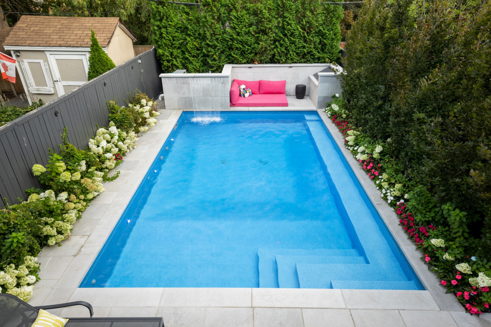 Small contemporary back rectangular swimming pool in Toronto with with pool landscaping and natural stone paving.