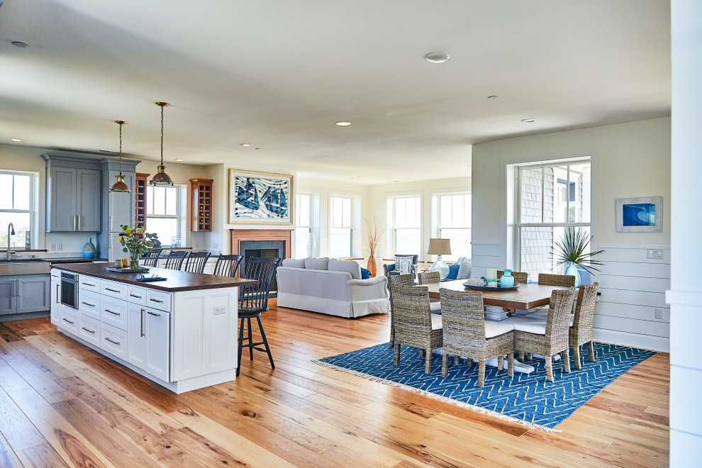 Mid-sized beach style open plan dining in Other with beige walls, light hardwood floors, a standard fireplace, a concrete fireplace surround and brown floor.