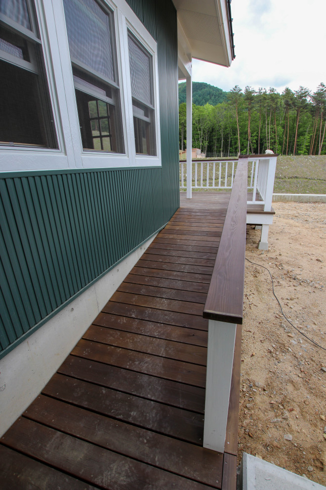 Expansive scandinavian ground level deck in Other with a roof extension and wood railing.