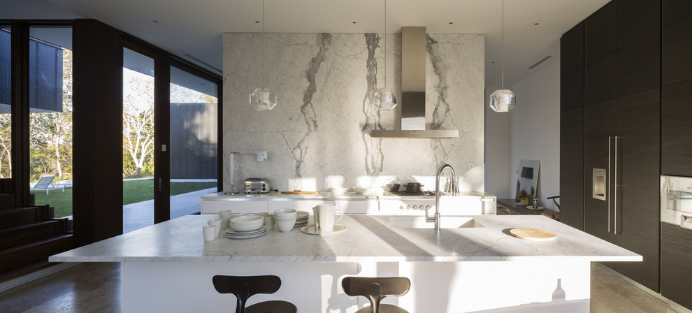 Large modern l-shaped eat-in kitchen in New York with limestone floors, with island, an undermount sink, flat-panel cabinets, white cabinets, marble benchtops, white splashback, stone slab splashback, panelled appliances and beige floor.