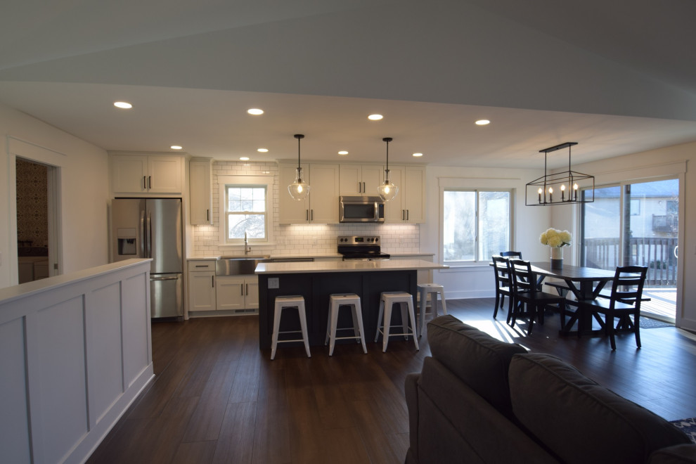 Open concept kitchen - mid-sized transitional single-wall vinyl floor open concept kitchen idea with a farmhouse sink, shaker cabinets, quartz countertops, white backsplash, subway tile backsplash, stainless steel appliances, an island and white countertops