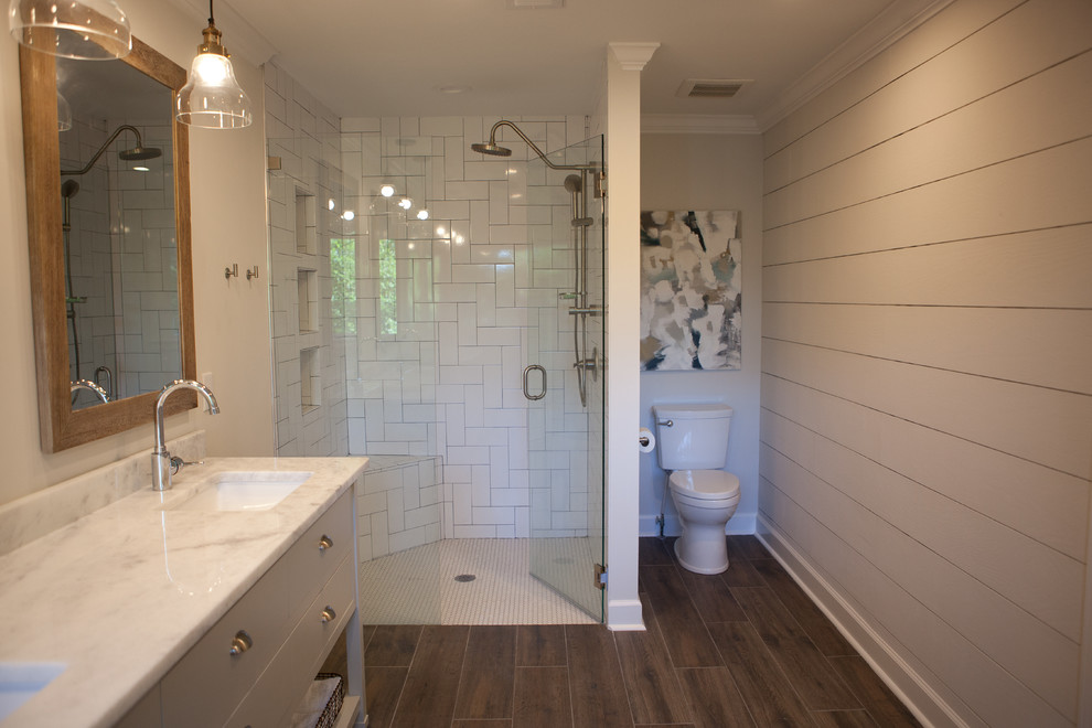 Large modern master bathroom in Atlanta with white cabinets, a corner shower, a one-piece toilet, white tile, subway tile, dark hardwood floors, marble benchtops, grey walls, brown floor, a hinged shower door, an undermount sink and flat-panel cabinets.