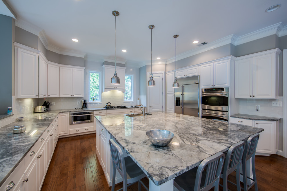 Photo of a large arts and crafts u-shaped open plan kitchen in DC Metro with an undermount sink, white cabinets, marble benchtops, white splashback, ceramic splashback, stainless steel appliances, medium hardwood floors, with island, recessed-panel cabinets and brown floor.