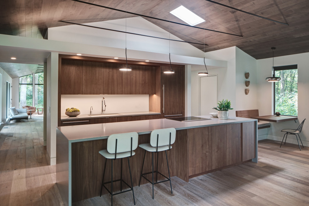 Design ideas for a midcentury kitchen in Chicago with flat-panel cabinets, dark wood cabinets, grey splashback, light hardwood floors, with island and grey benchtop.