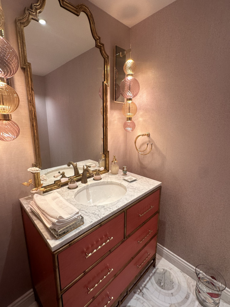 На фото: туалет среднего размера в стиле неоклассика (современная классика) с фасадами островного типа, красными фасадами, унитазом-моноблоком, разноцветной плиткой, розовыми стенами, мраморным полом, врезной раковиной, мраморной столешницей, белым полом, белой столешницей, встроенной тумбой и обоями на стенах
