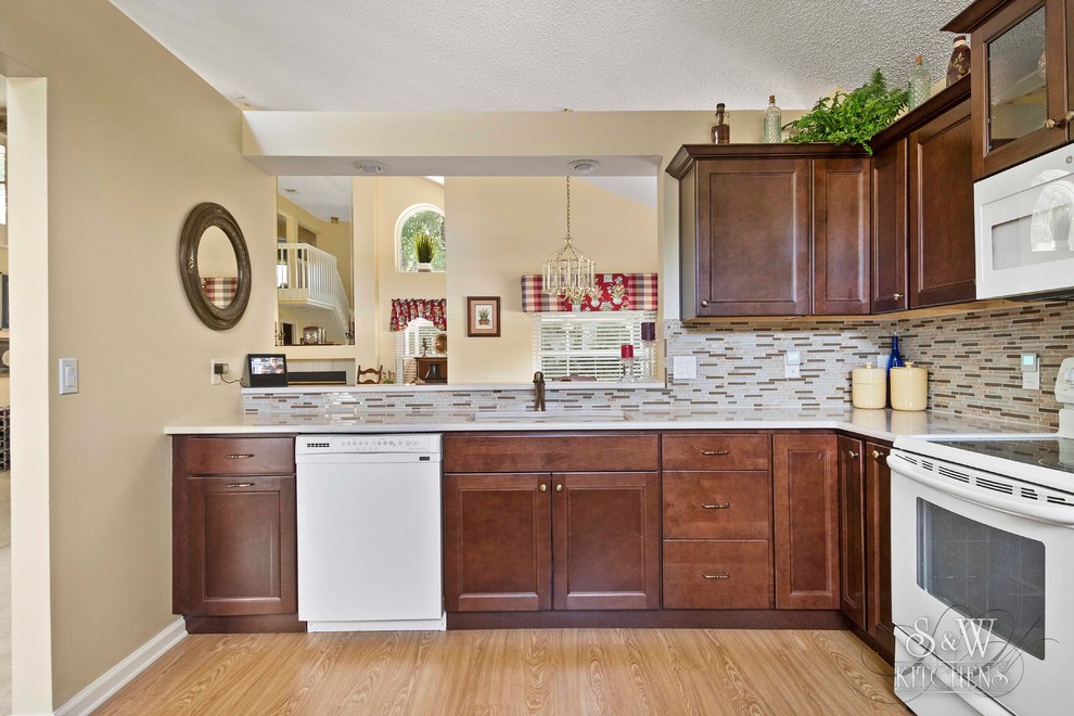 Inspiration for a traditional l-shaped kitchen in Orlando with a double-bowl sink, recessed-panel cabinets, brown cabinets, quartz benchtops, beige splashback, glass tile splashback, white appliances and vinyl floors.