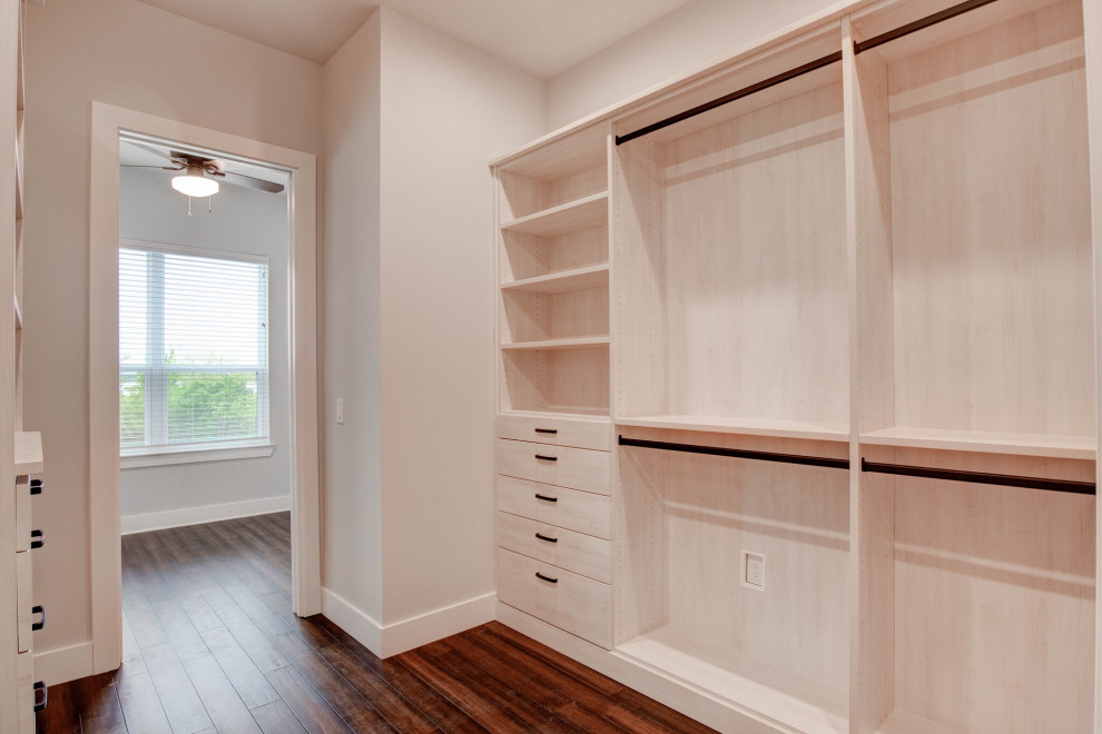 Large transitional gender-neutral walk-in wardrobe in Dallas with flat-panel cabinets, light wood cabinets, laminate floors and brown floor.