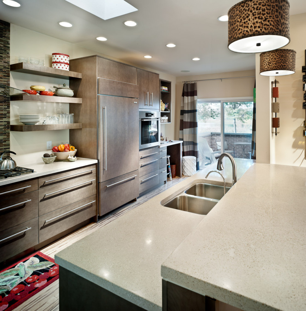 This is an example of a transitional kitchen in Other with a double-bowl sink, flat-panel cabinets, brown cabinets, concrete benchtops, glass tile splashback, stainless steel appliances, bamboo floors, a peninsula, multi-coloured floor and beige benchtop.
