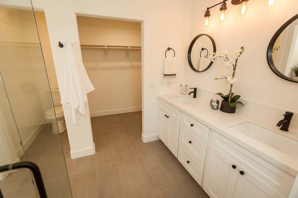 Photo of a mid-sized country 3/4 bathroom in San Luis Obispo with shaker cabinets, white cabinets, an alcove shower, white tile, porcelain tile, white walls, ceramic floors, an undermount sink, engineered quartz benchtops, grey floor, a hinged shower door and white benchtops.
