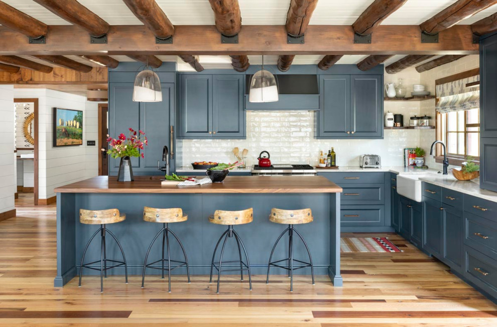 Пример оригинального дизайна: кухня в стиле рустика с с полувстраиваемой мойкой (с передним бортиком), синими фасадами, белым фартуком, светлым паркетным полом, белой столешницей и балками на потолке