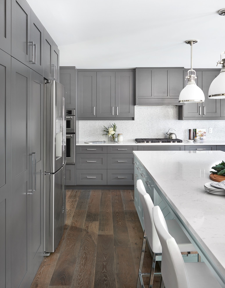 Design ideas for a transitional l-shaped kitchen in Toronto with shaker cabinets, grey cabinets, white splashback, stainless steel appliances, dark hardwood floors, with island, brown floor and white benchtop.