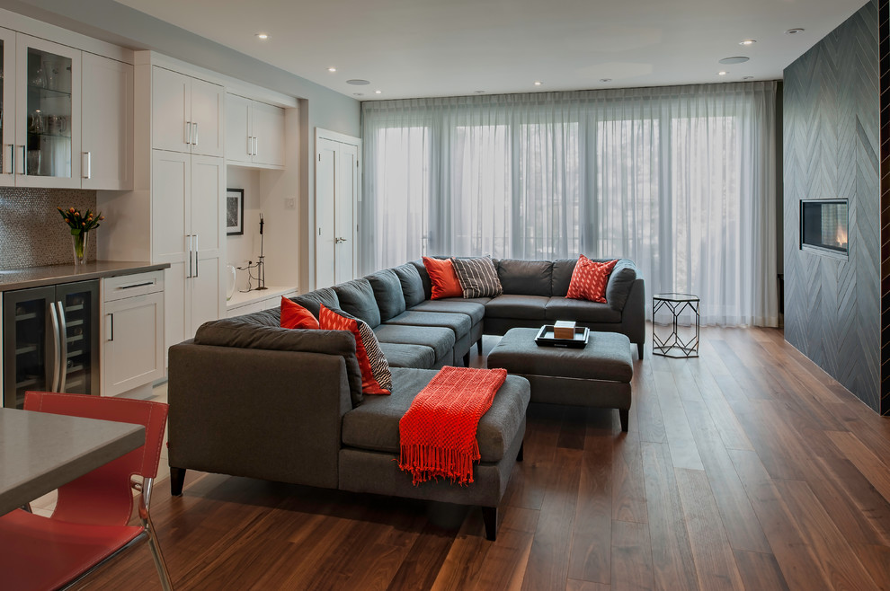Photo of a large modern open concept family room in Toronto with a home bar, grey walls, medium hardwood floors, a ribbon fireplace, a tile fireplace surround, brown floor and a wall-mounted tv.