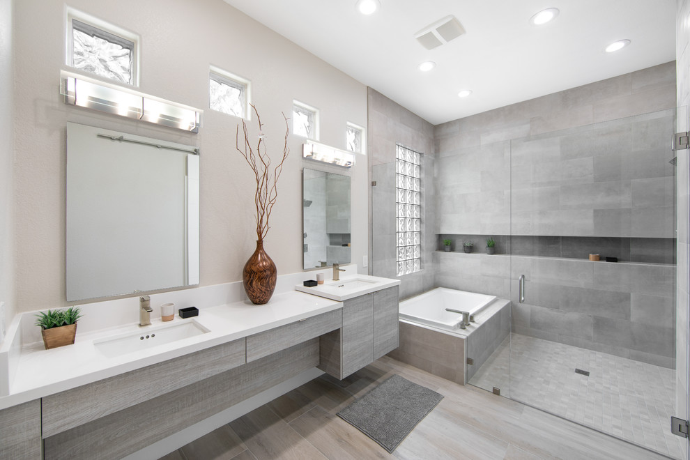 This is an example of a large contemporary wet room bathroom in Las Vegas with flat-panel cabinets, grey cabinets, a drop-in tub, gray tile, grey walls, an undermount sink, grey floor, a hinged shower door, white benchtops and a niche.