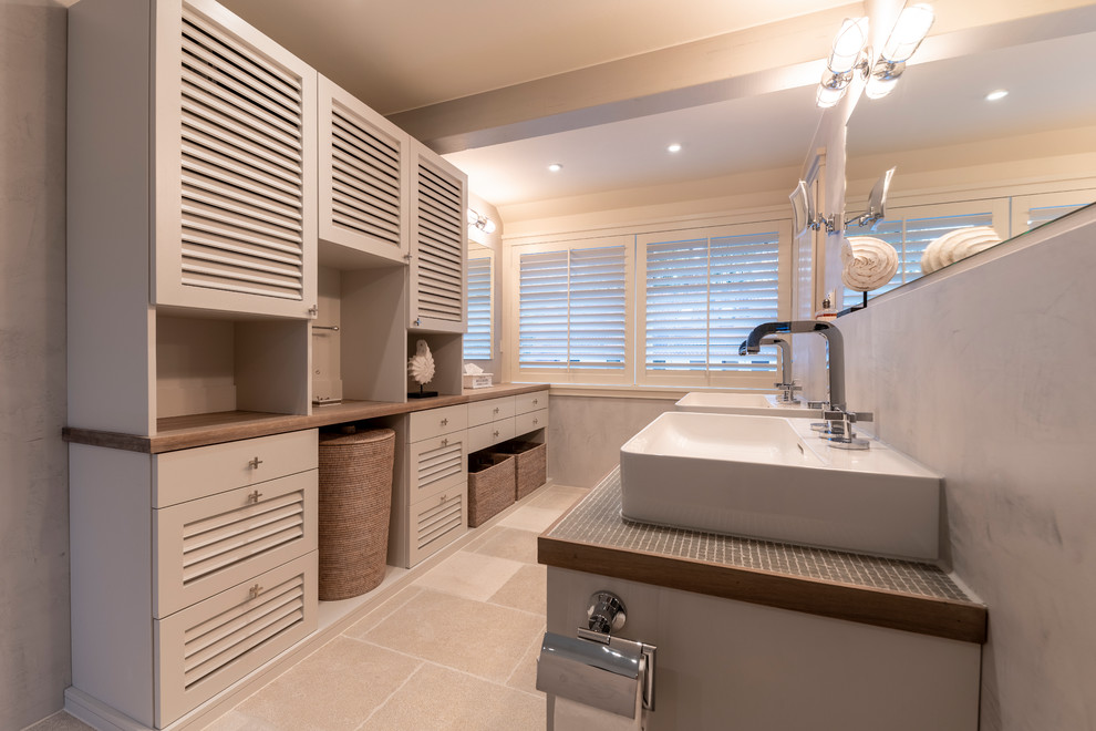 This is an example of a large country master bathroom in Frankfurt with louvered cabinets, grey cabinets, a curbless shower, a wall-mount toilet, grey walls, limestone floors, a vessel sink, tile benchtops, beige floor, an open shower and grey benchtops.