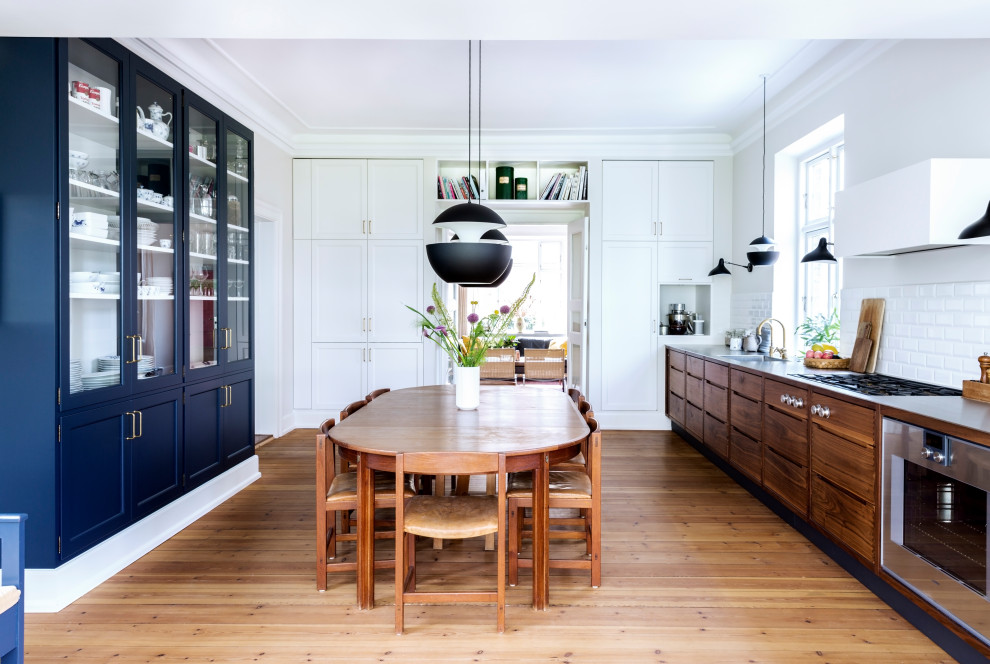 Photo of a contemporary u-shaped eat-in kitchen in Odense with an integrated sink, flat-panel cabinets, dark wood cabinets, stainless steel benchtops, white splashback, subway tile splashback, stainless steel appliances, medium hardwood floors, no island, brown floor and grey benchtop.