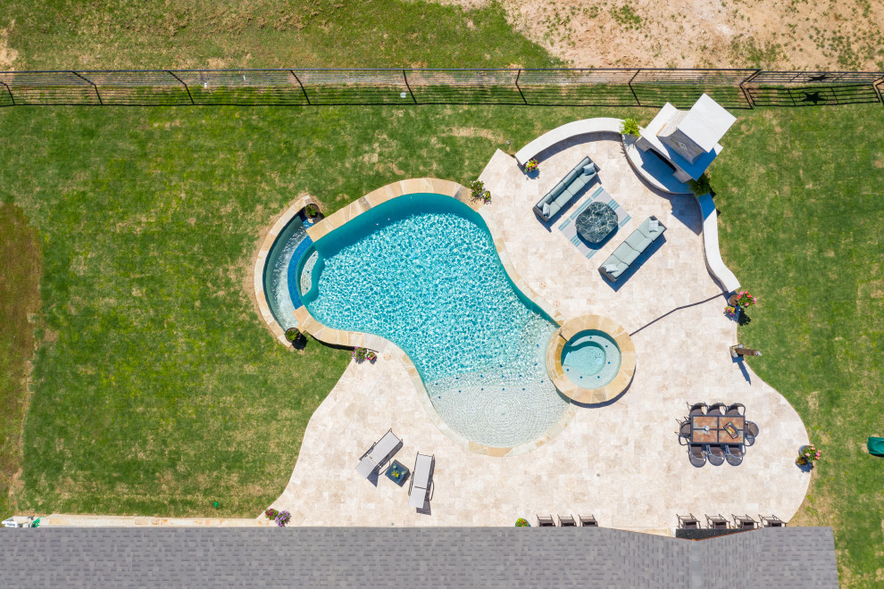This is an example of a large traditional backyard custom-shaped infinity pool in Dallas with a hot tub and natural stone pavers.