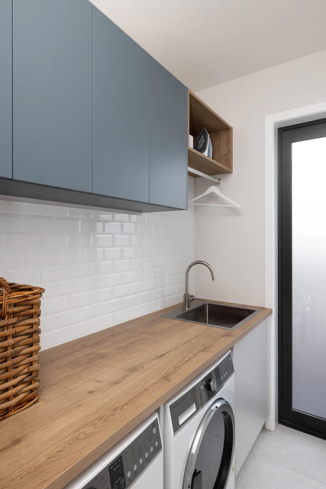 This is an example of a medium sized contemporary single-wall separated utility room in Auckland with white splashback, ceramic splashback, white worktops, a built-in sink, flat-panel cabinets, grey cabinets, wood worktops, white walls, porcelain flooring and a side by side washer and dryer.