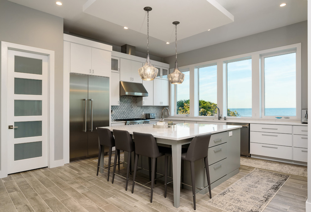Photo of a mid-sized contemporary l-shaped eat-in kitchen in Jacksonville with flat-panel cabinets, white cabinets, grey splashback, limestone splashback, stainless steel appliances, ceramic floors, with island, grey floor and white benchtop.