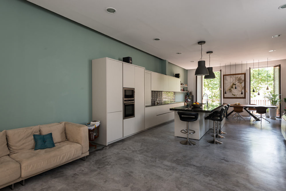 Photo of a large industrial single-wall open plan kitchen in Barcelona with a single-bowl sink, flat-panel cabinets, white cabinets, marble benchtops, grey splashback, porcelain splashback, stainless steel appliances, concrete floors, with island and grey floor.