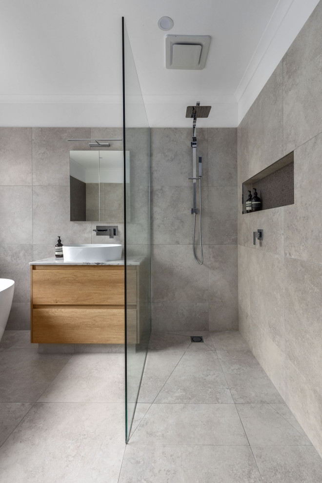 Idéer för att renovera ett mellanstort funkis vit vitt en-suite badrum, med släta luckor, skåp i ljust trä, ett fristående badkar, en dusch i en alkov, grå kakel, porslinskakel, grå väggar, klinkergolv i porslin, ett fristående handfat, bänkskiva i kvarts, grått golv och dusch med skjutdörr