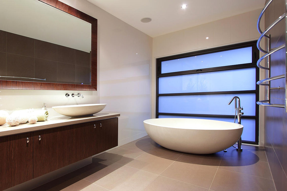 Photo of a large master bathroom in Melbourne with a vessel sink, dark wood cabinets, granite benchtops, a freestanding tub, beige tile, ceramic tile, beige walls and ceramic floors.