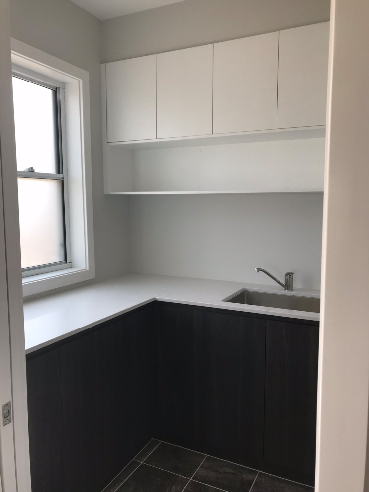 Design ideas for a mid-sized beach style u-shaped dedicated laundry room in Central Coast with an undermount sink, quartz benchtops, grey walls, porcelain floors, a stacked washer and dryer, grey floor and white benchtop.