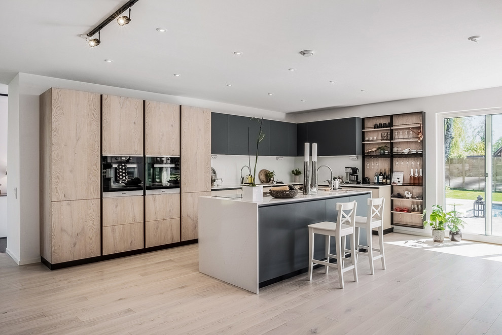 This is an example of a scandinavian l-shaped kitchen in Malmo with flat-panel cabinets, black cabinets, black appliances, light hardwood floors, with island, beige floor and white benchtop.