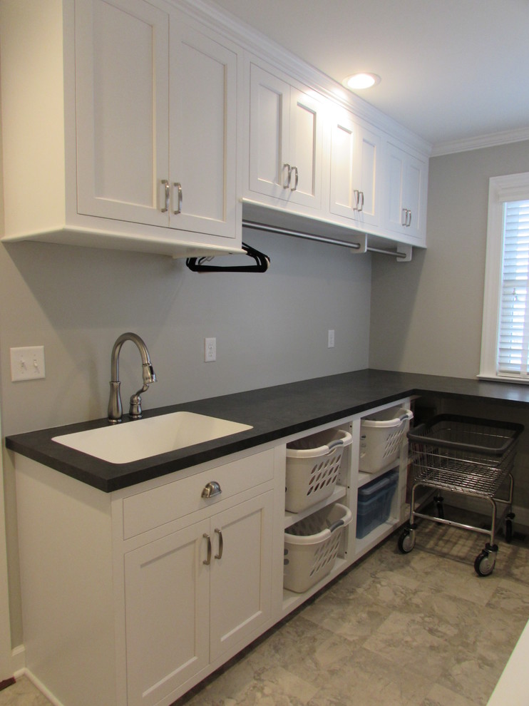 Mid-sized transitional single-wall dedicated laundry room in DC Metro with an undermount sink, recessed-panel cabinets, white cabinets, solid surface benchtops, white walls, ceramic floors, a side-by-side washer and dryer and black benchtop.