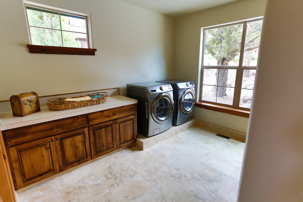 Photo of a large traditional galley utility room in Other with raised-panel cabinets, medium wood cabinets, tile benchtops, white walls and a side-by-side washer and dryer.