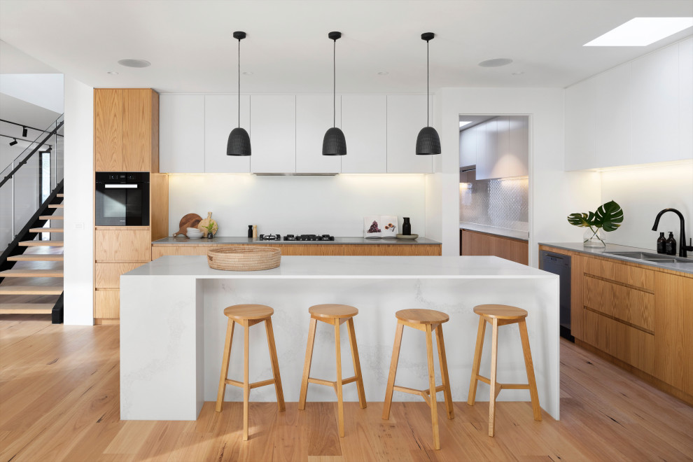 Modern inredning av ett vit vitt kök, med en dubbel diskho, släta luckor, skåp i mellenmörkt trä, bänkskiva i kvarts, vitt stänkskydd, rostfria vitvaror, mellanmörkt trägolv, en köksö och brunt golv