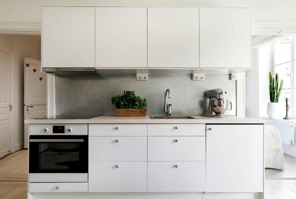 This is an example of a mid-sized scandinavian single-wall open plan kitchen in Stockholm with a drop-in sink, flat-panel cabinets, white cabinets, wood benchtops, grey splashback, light hardwood floors and no island.