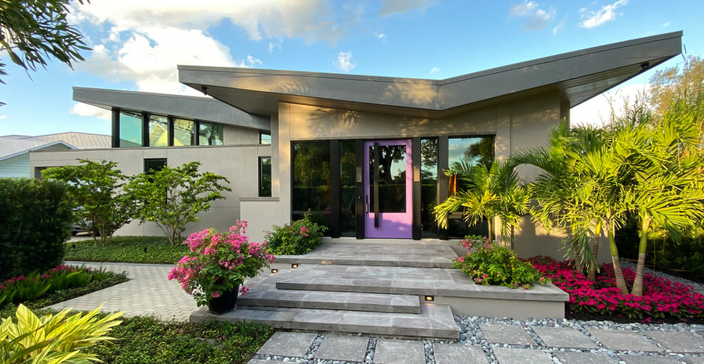 Photo of a mid-sized midcentury one-storey stucco grey house exterior in Other with a butterfly roof, a mixed roof and a grey roof.
